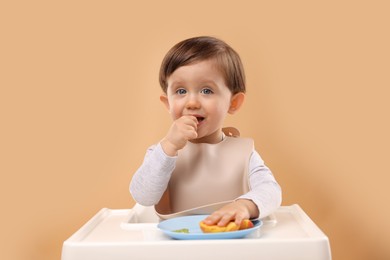 Photo of Healthy baby food. Cute little kid eating fruits in high chair on beige background