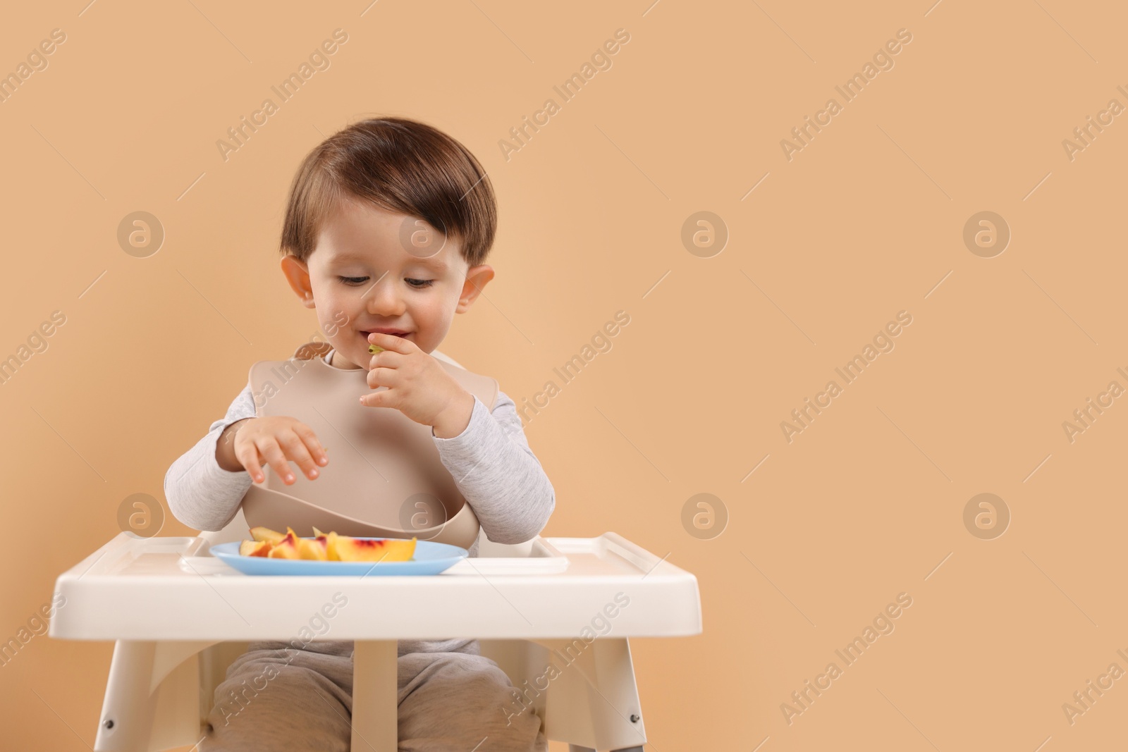 Photo of Healthy baby food. Cute little kid eating fruits in high chair on beige background, space for text