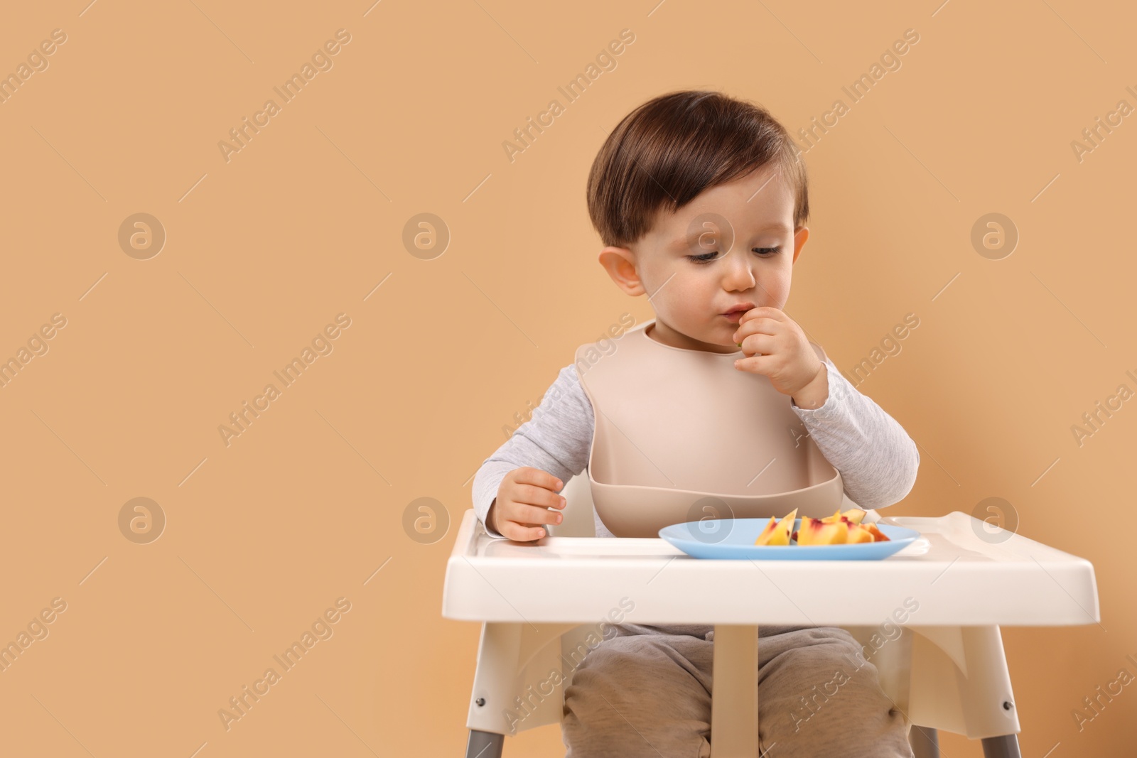 Photo of Healthy baby food. Cute little kid eating fruits in high chair on beige background, space for text