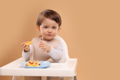 Photo of Healthy baby food. Cute little kid eating fruits in high chair on beige background, space for text