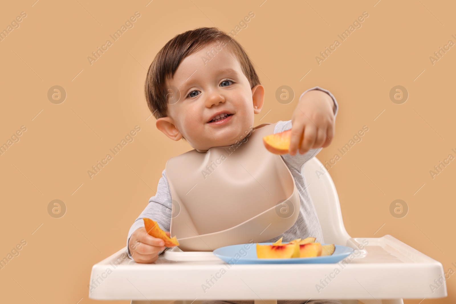 Photo of Healthy baby food. Cute little kid eating fruits in high chair on beige background