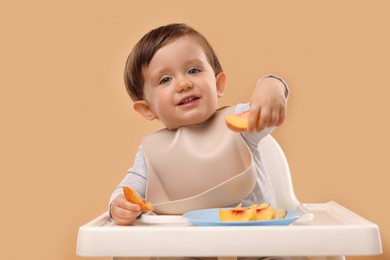 Photo of Healthy baby food. Cute little kid eating fruits in high chair on beige background