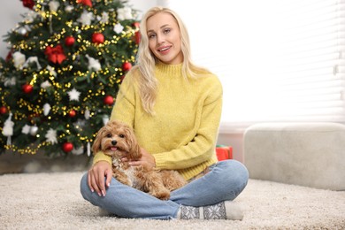 Photo of Woman with cute Maltipoo dog on rug in room decorated for Christmas