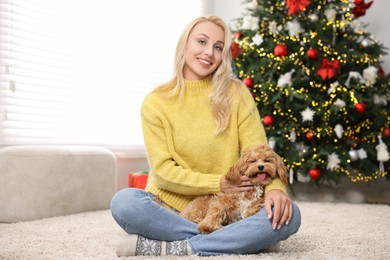 Photo of Woman with cute Maltipoo dog on rug in room decorated for Christmas