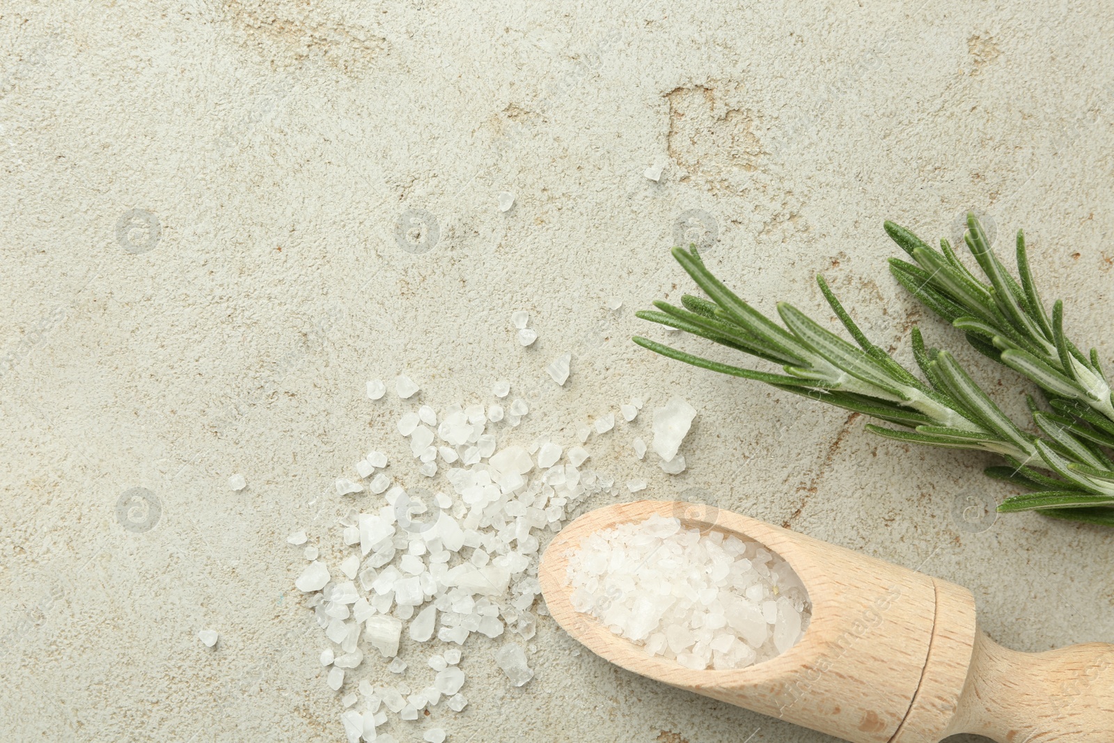 Photo of Sea salt in wooden scoop and rosemary on grey table, top view. Space for text