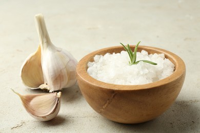 Photo of Sea salt in bowl, rosemary and garlic on grey table, closeup