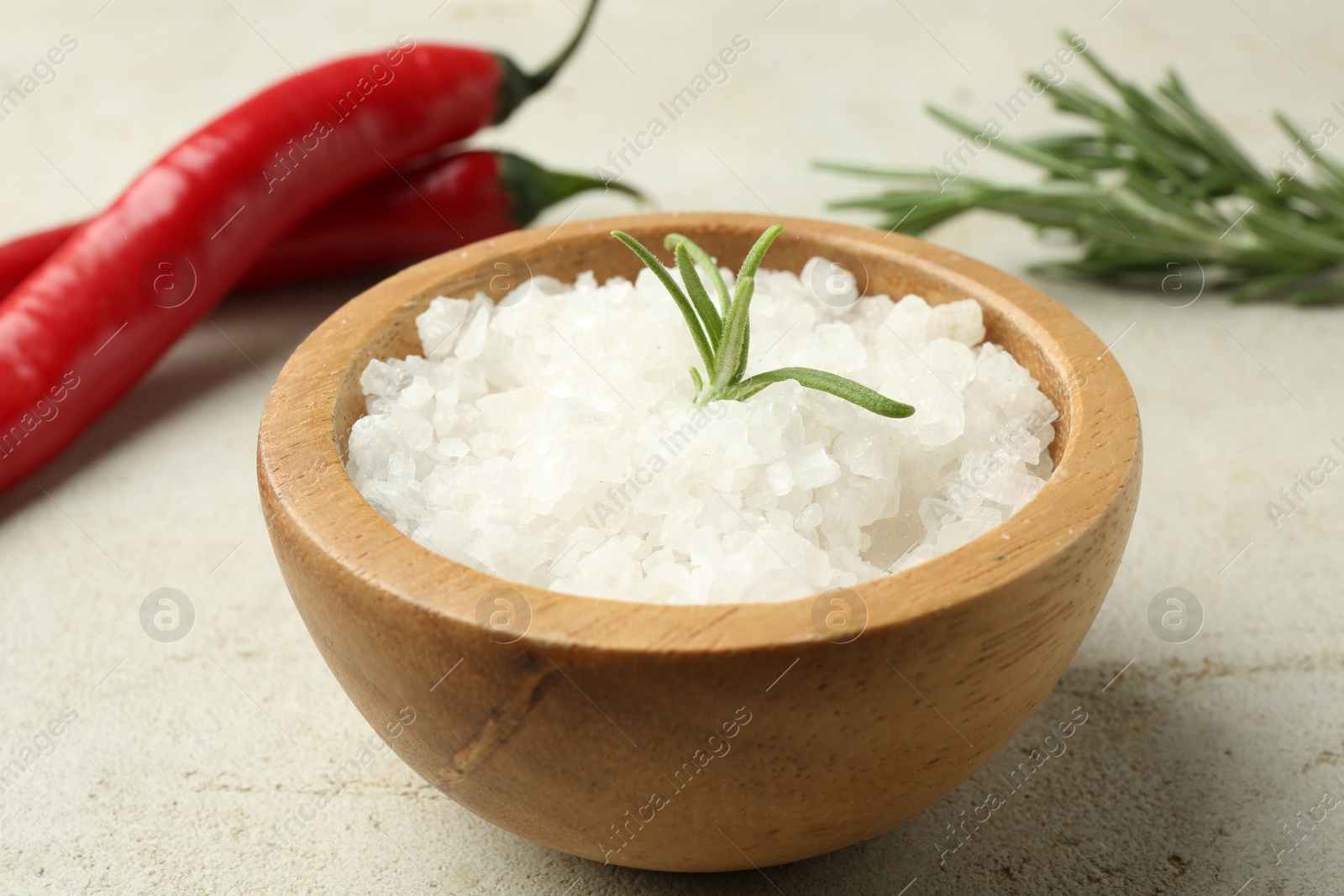 Photo of Sea salt in bowl, rosemary and chili peppers on grey table, closeup