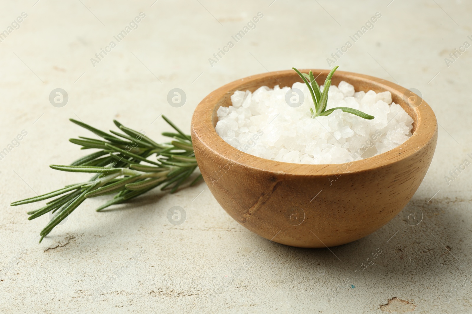 Photo of Sea salt in bowl and rosemary on grey table, closeup