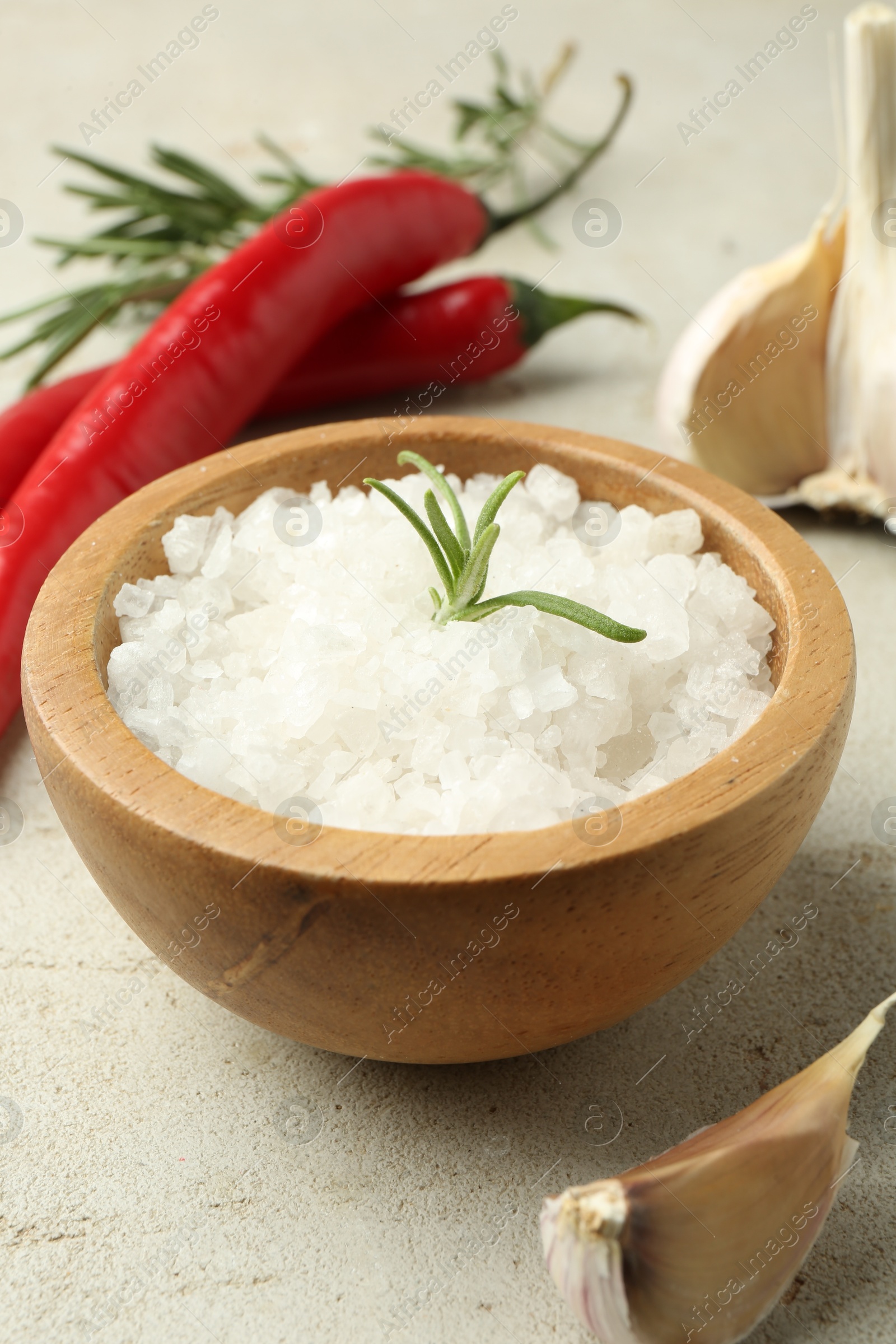 Photo of Sea salt in bowl, rosemary, chili peppers and garlic on grey table, closeup