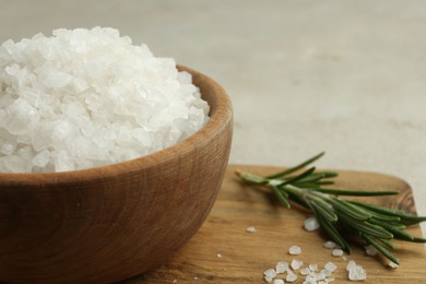 Sea salt in bowl and rosemary on table, closeup