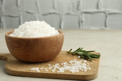 Photo of Sea salt in bowl and rosemary on grey table, closeup. Space for text