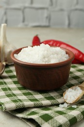 Photo of Sea salt in bowl, garlic and chili peppers on table, closeup