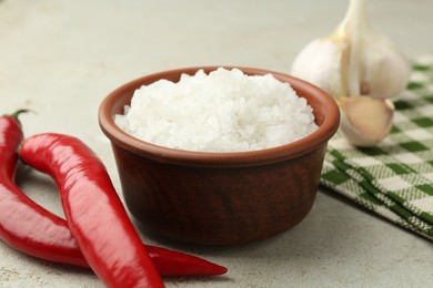 Photo of Sea salt in bowl, garlic and chili peppers on grey table, closeup