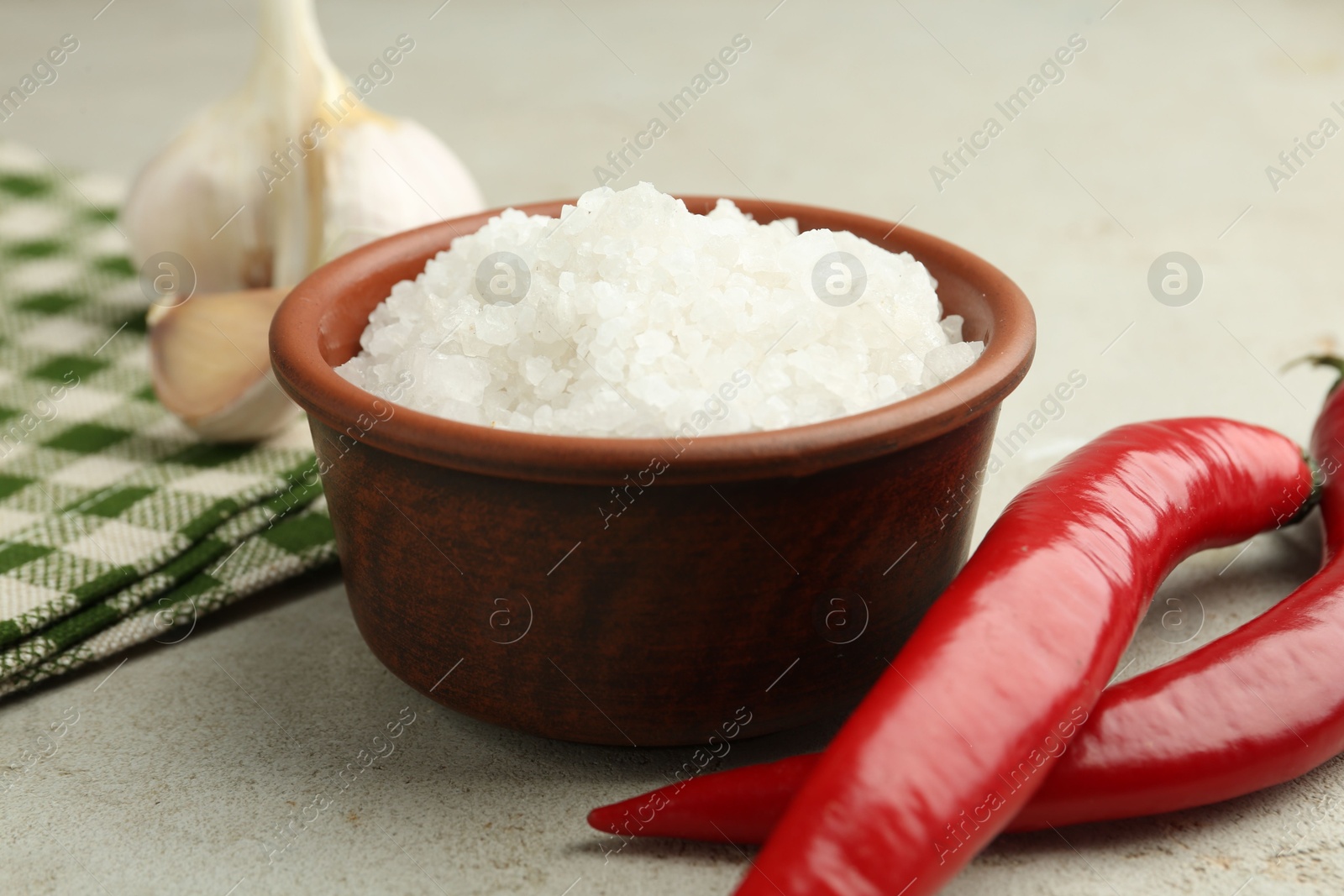 Photo of Sea salt in bowl, garlic and chili peppers on grey table, closeup