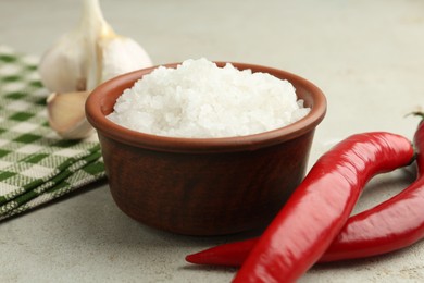 Sea salt in bowl, garlic and chili peppers on grey table, closeup