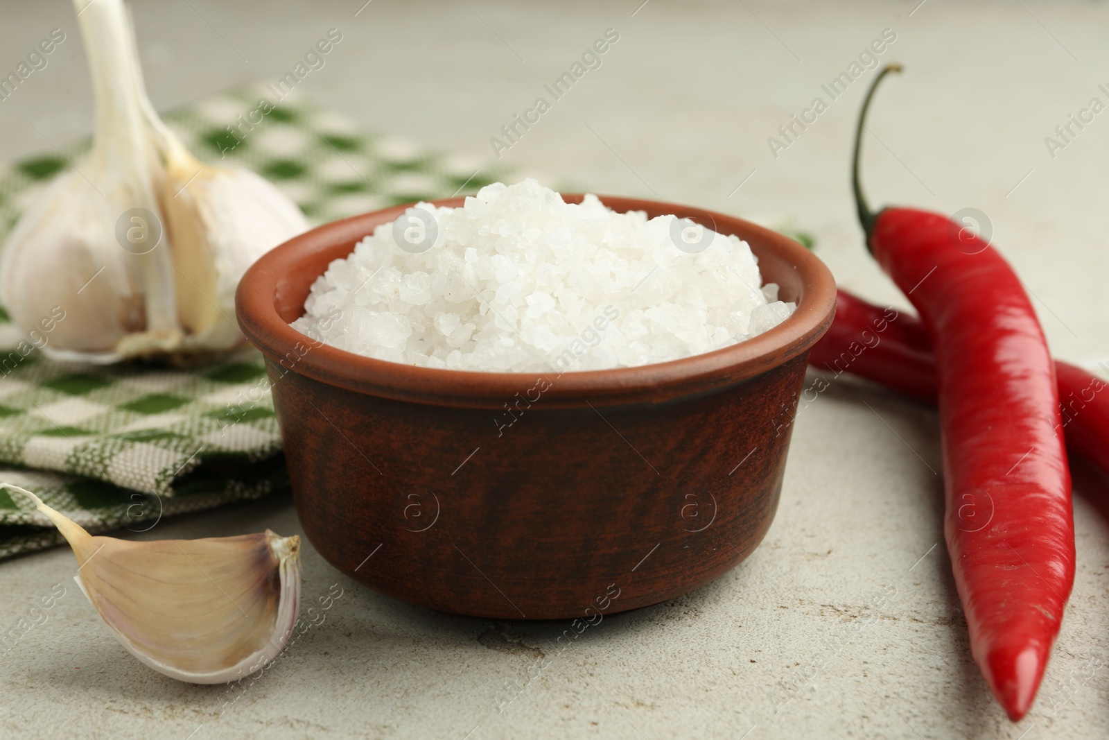 Photo of Sea salt in bowl, garlic and chili peppers on grey table, closeup