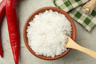 Photo of Sea salt in bowl, chili peppers and garlic on grey table, top view