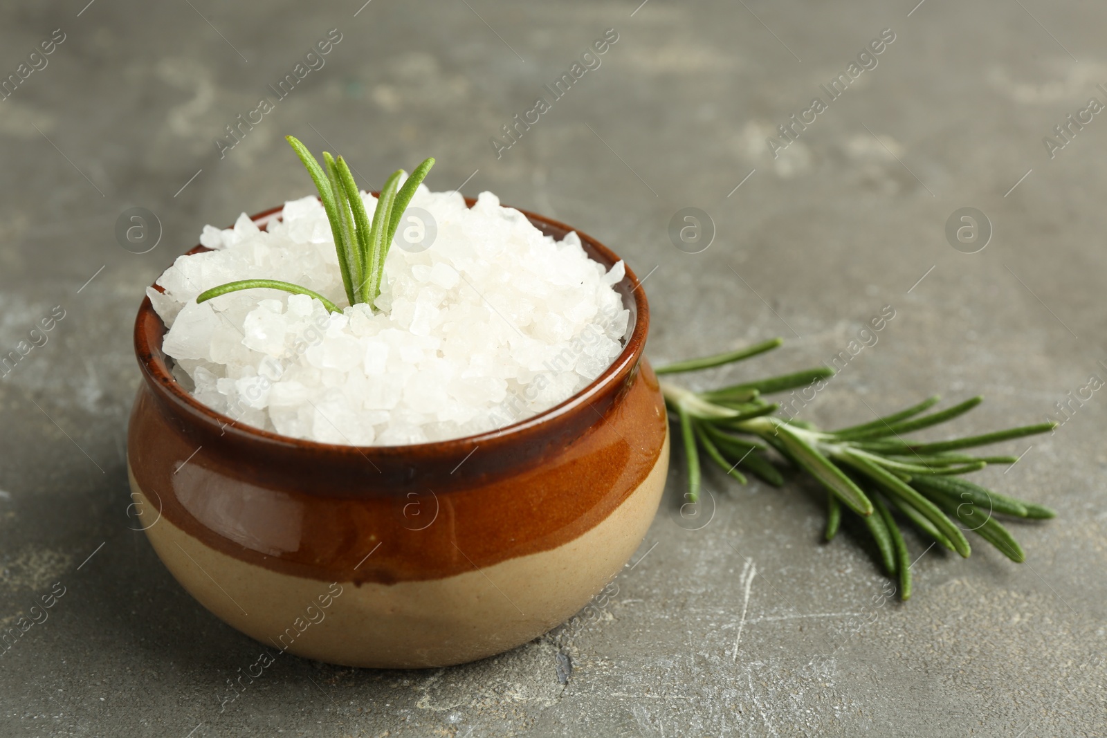 Photo of Sea salt in bowl and rosemary on grey table, closeup