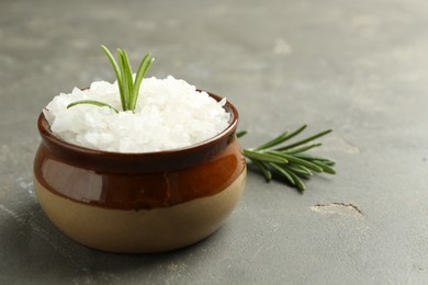 Photo of Sea salt in bowl and rosemary on grey table, closeup. Space for text