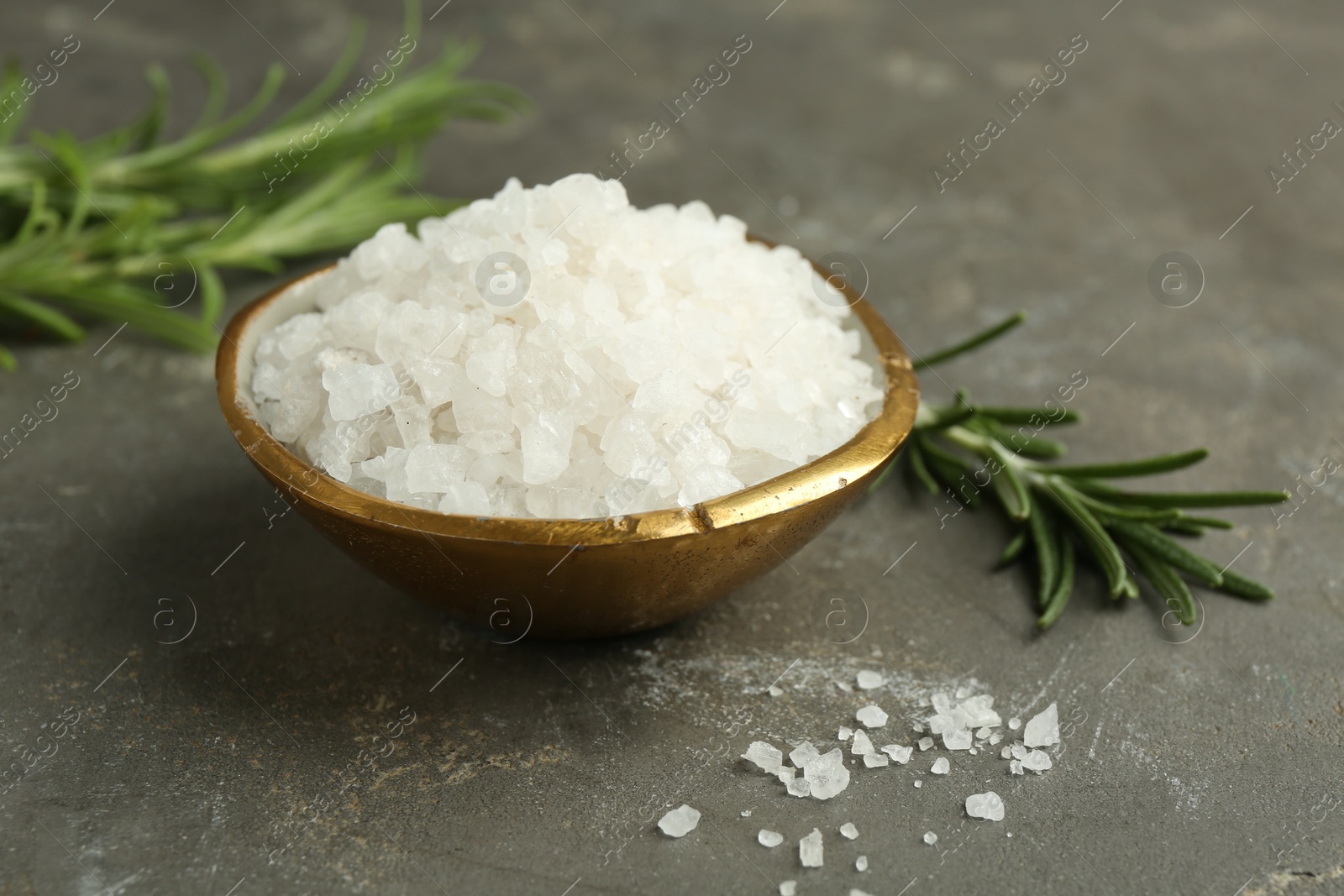 Photo of Sea salt in bowl and rosemary on grey table, closeup