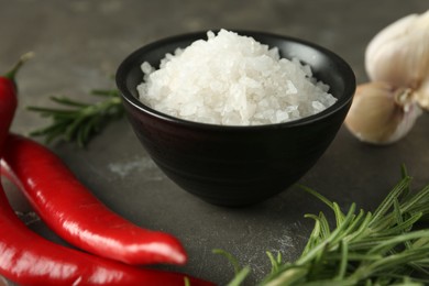 Sea salt in bowl, rosemary, chili peppers and garlic on grey table, closeup