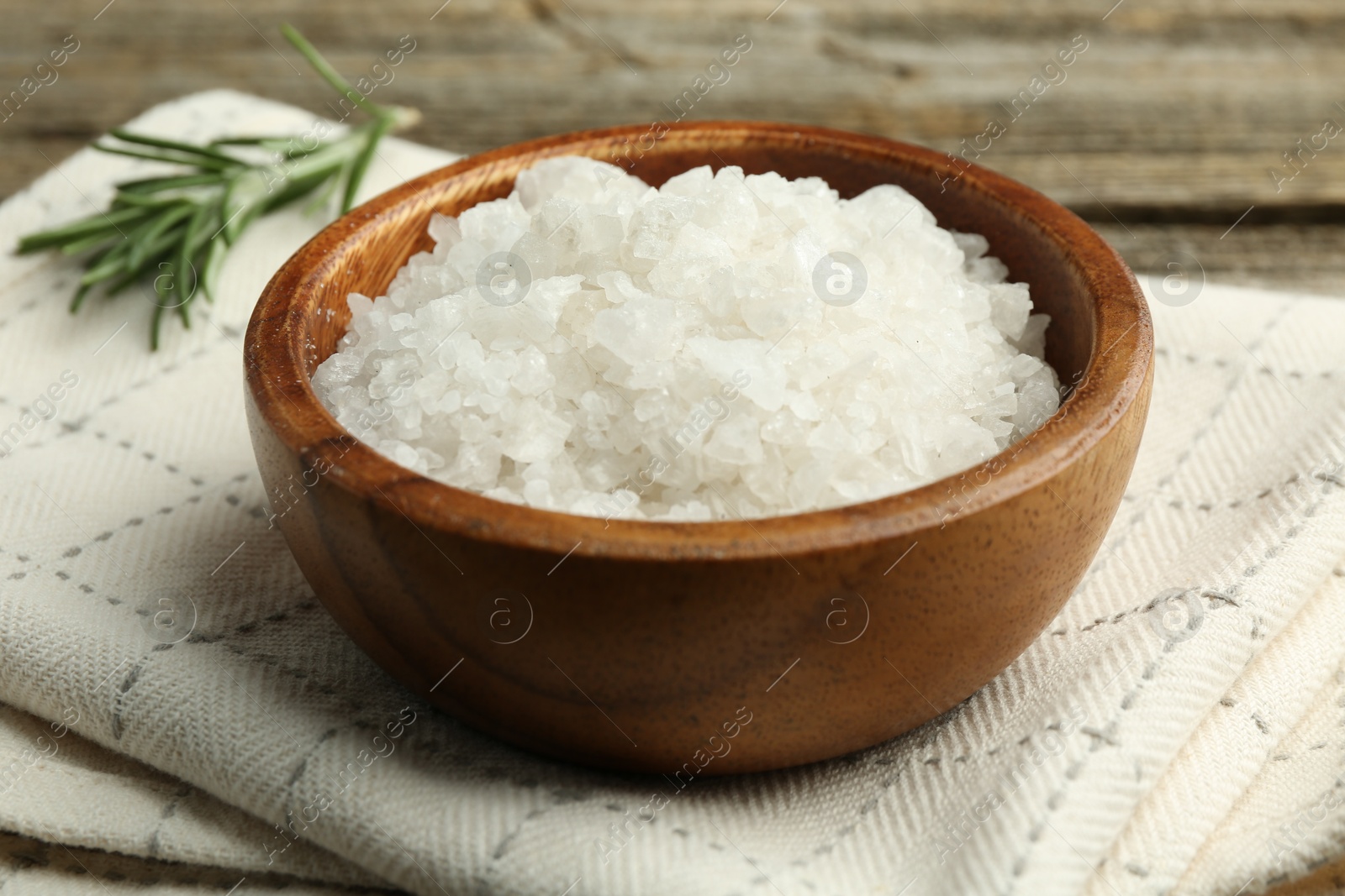 Photo of Sea salt in bowl and rosemary on table, closeup