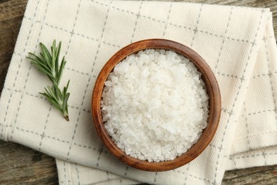 Sea salt in bowl and rosemary on wooden table, top view