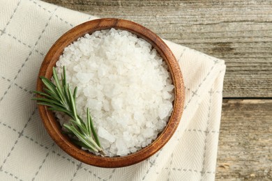 Sea salt in bowl and rosemary on wooden table, top view