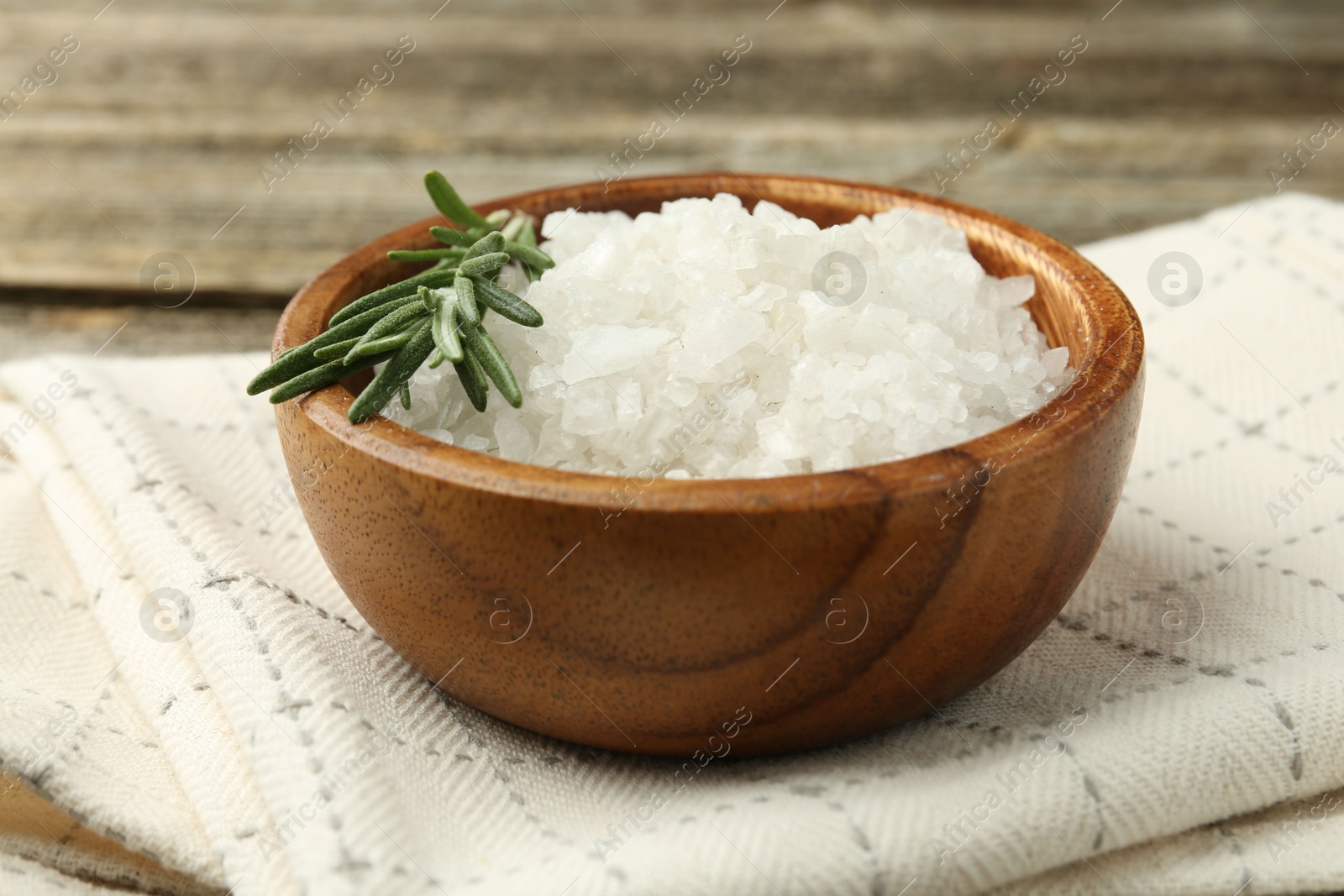 Photo of Sea salt in bowl and rosemary on table, closeup