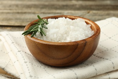 Photo of Sea salt in bowl and rosemary on table, closeup