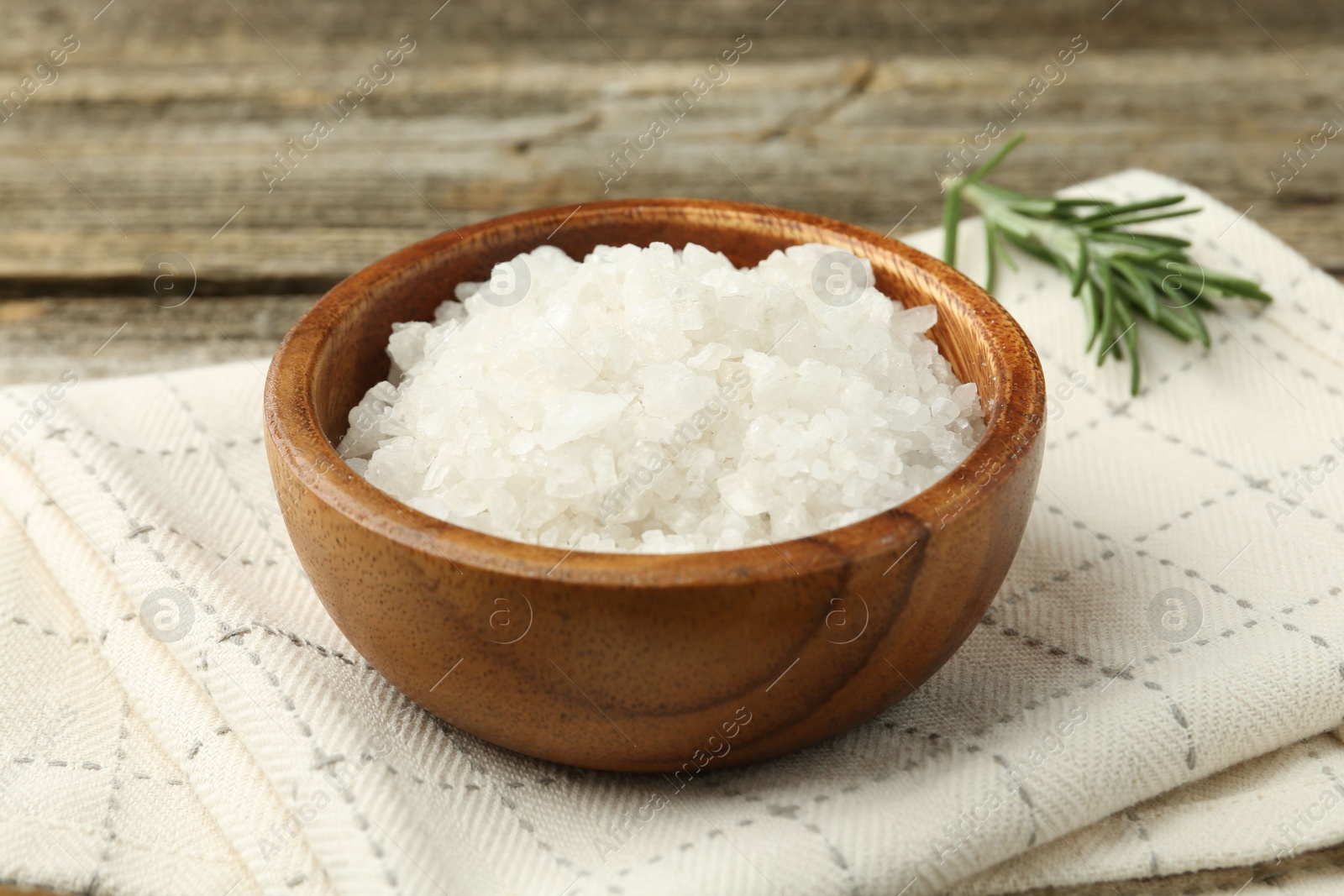 Photo of Sea salt in bowl and rosemary on table, closeup