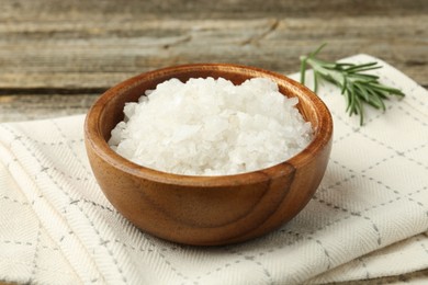 Photo of Sea salt in bowl and rosemary on table, closeup