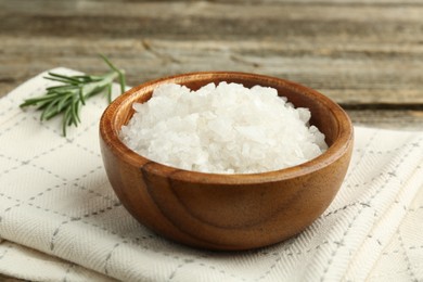 Photo of Sea salt in bowl and rosemary on table, closeup