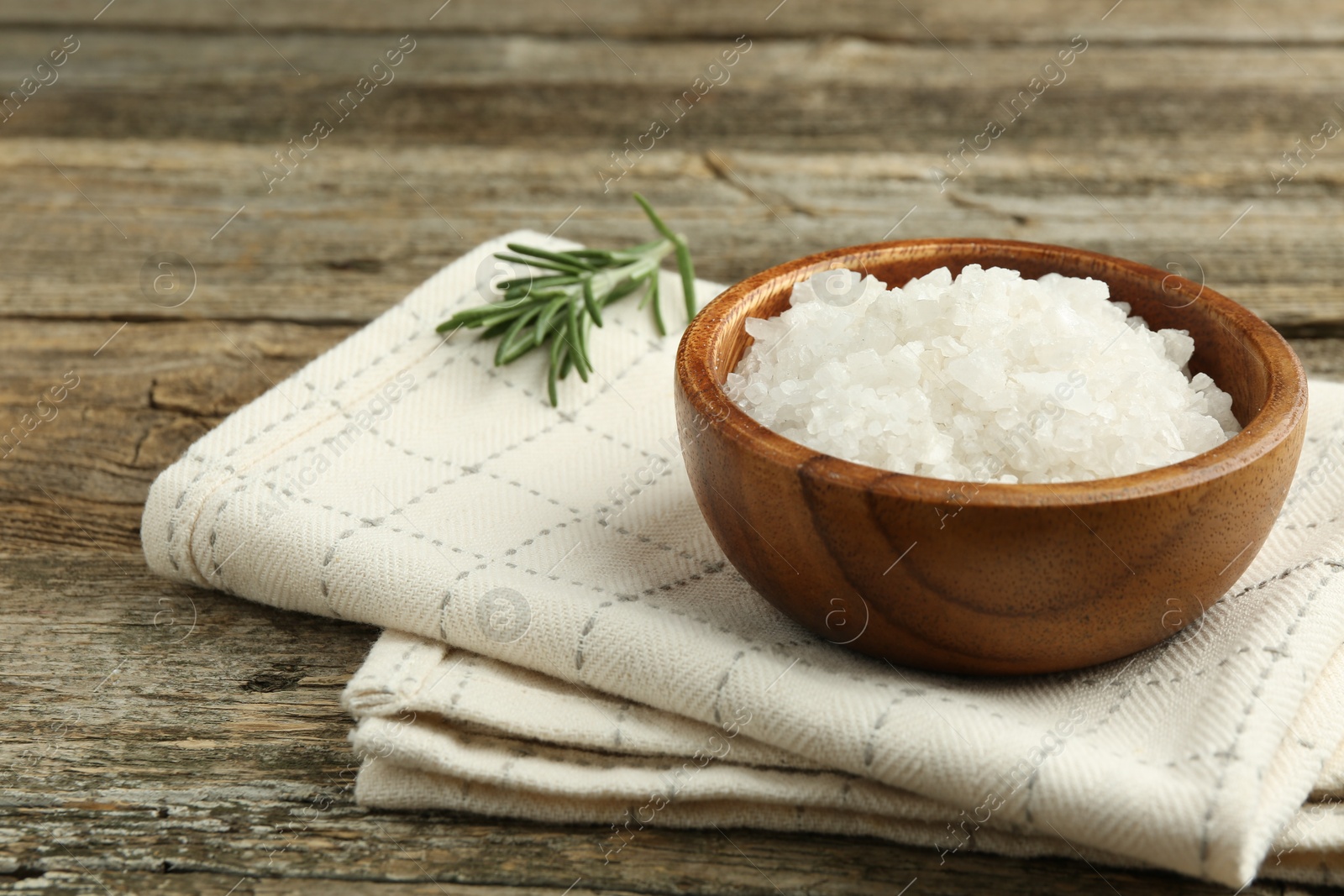 Photo of Sea salt in bowl and rosemary on wooden table, closeup