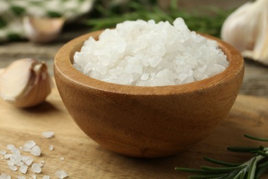 Photo of Sea salt in bowl, rosemary and garlic on table, closeup