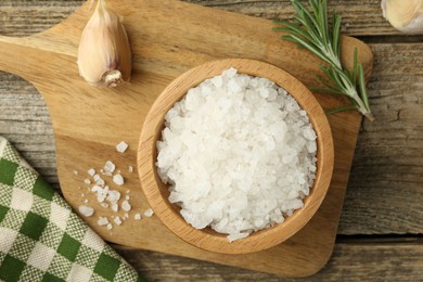 Sea salt in bowl, rosemary and garlic on wooden table, top view