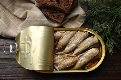 Photo of Tasty sprats in tin can, dill and bread on wooden table, top view