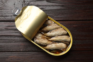 Tasty sprats in tin can on wooden table, top view