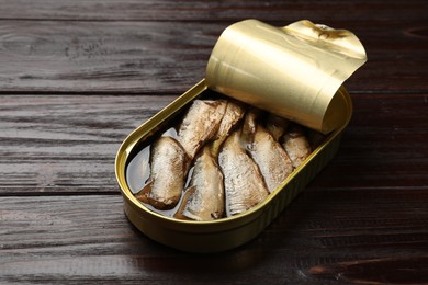 Photo of Tasty sprats in tin can on wooden table, closeup