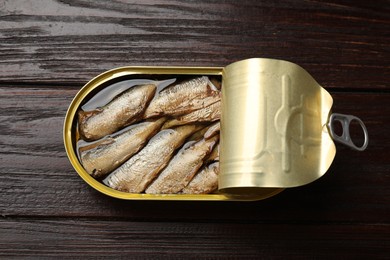 Tasty sprats in tin can on wooden table, top view