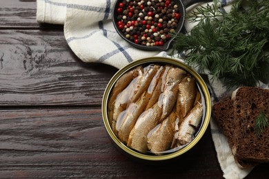 Photo of Tasty sprats in tin can, peppercorns, bread and dill on wooden table, top view. Space for text