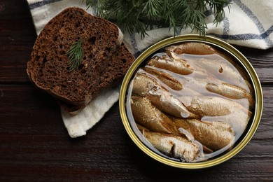 Tasty sprats in tin can, dill and bread on wooden table, top view