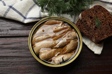 Tasty sprats in tin can, dill and bread on wooden table, top view