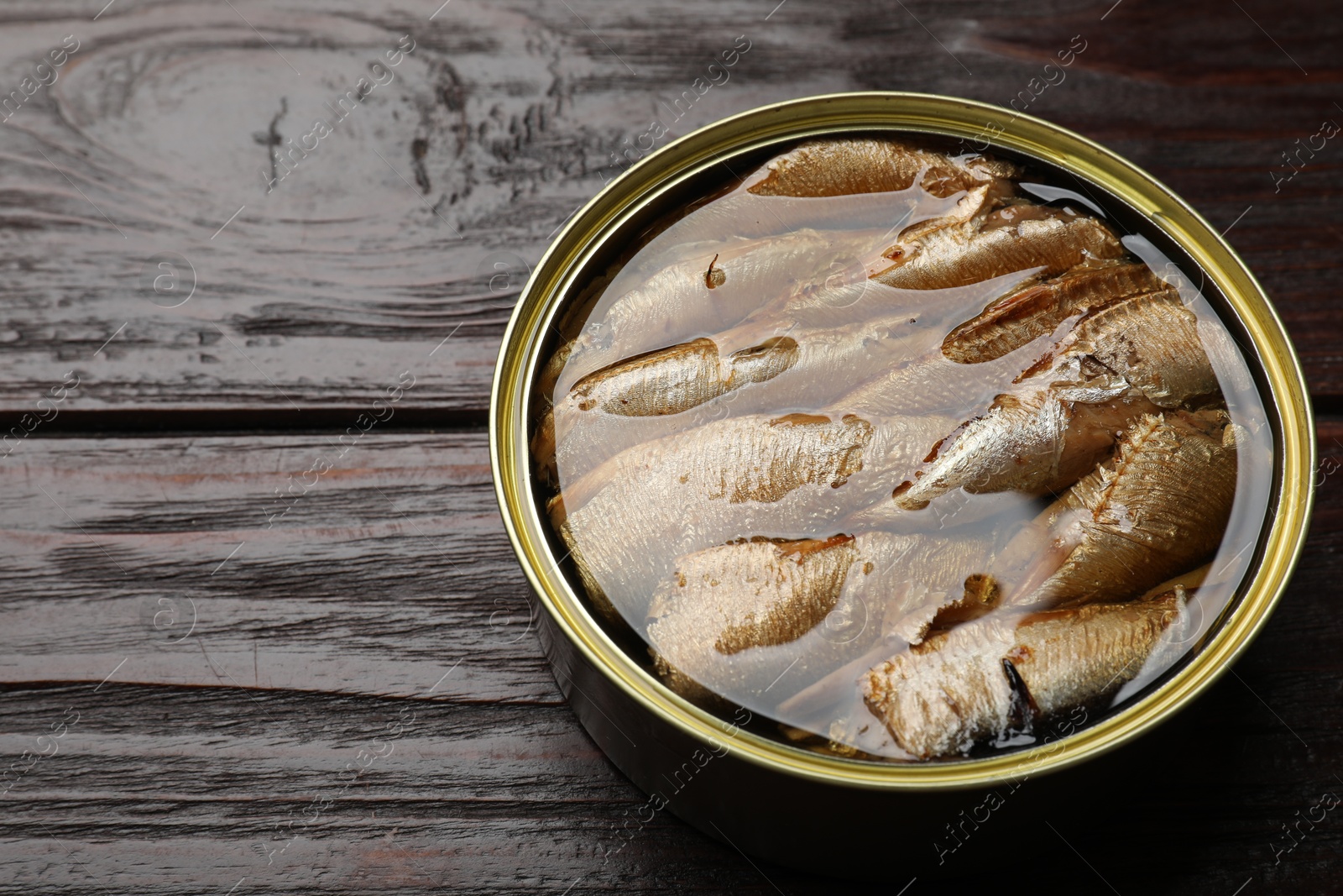 Photo of Tasty sprats in tin can on wooden table, closeup. Space for text