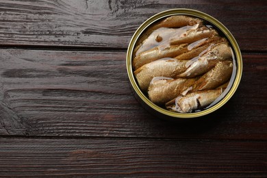 Tasty sprats in tin can on wooden table, above view. Space for text