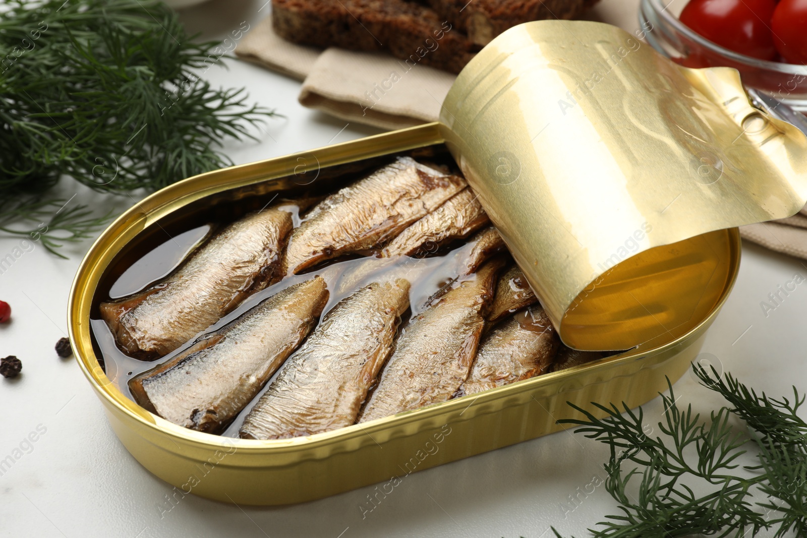 Photo of Tasty sprats in tin can and dill on white table, closeup