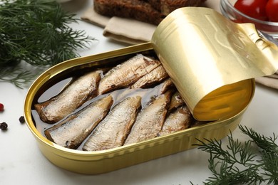 Tasty sprats in tin can and dill on white table, closeup