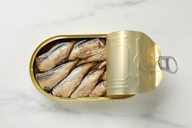 Tasty sprats in tin can on white marble table, top view