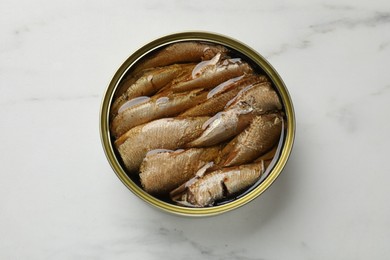 Tasty sprats in tin can on white marble table, top view