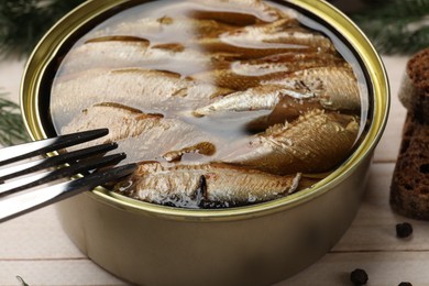 Photo of Tasty sprats in tin can and fork on wooden table, closeup